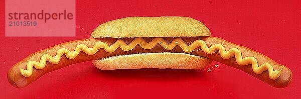 Bockwurst sausage with mustard in a roll against a red background