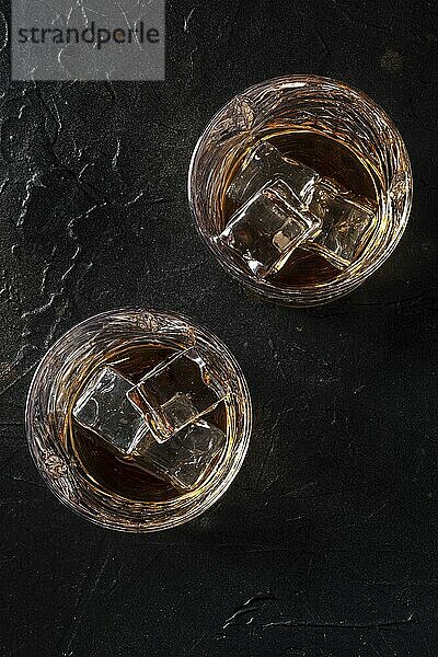 Whiskey in glasses with ice. Bourbon whisky on rocks on a black slate background  shot from above