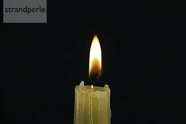 Burning yellow wax candle contrasting with the dark background  candle's gentle flame suggesting of remembrance  reflection and hope