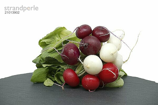 Radish with leaves on black slate serving bosrd over white background. European radishes (Raphanus sativus)