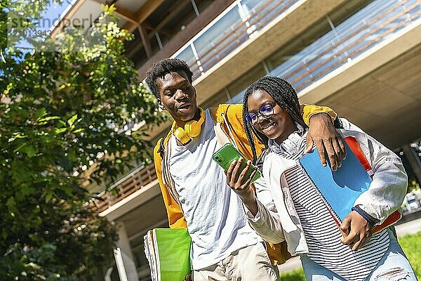 Low angle view portrait of a young casual african couple embracing while using phone in the university campus