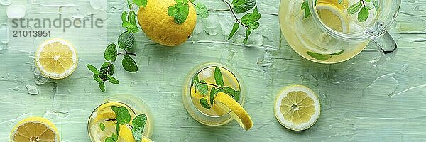 Lemonade with mint panoramic banner. Lemon water drink with ice. Two glasses and a pitcher on a blue background  overhead flat lay shot. Detox beverage. Fresh homemade cocktail