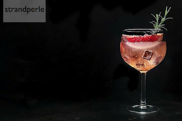 Fancy cocktail with fresh fruit. Gin and tonic drink with ice at a party  on a black background. Alcohol with pink grapefruit and rosemary  with a place for text  Food photography  Food photography