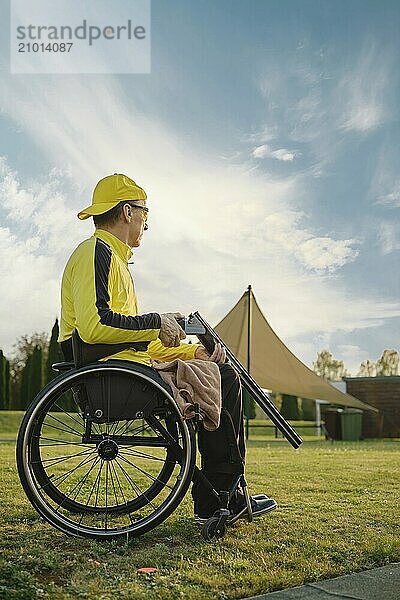 An elderly man with paralysed legs in a wheelchair opens his hunting rifle to reload the ammunition