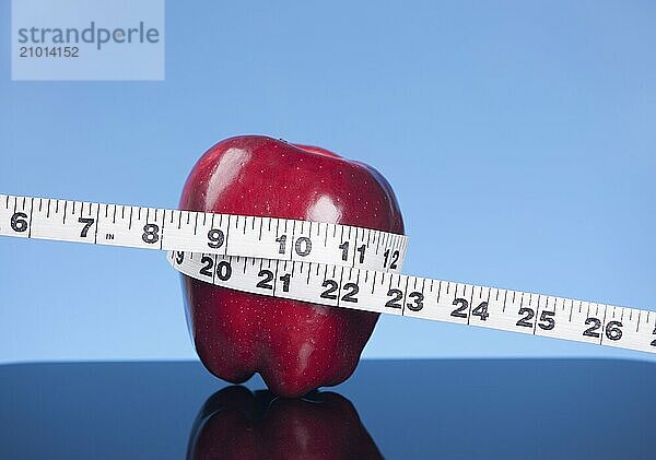 A concept image of an apple with a tape measure wrapped around it against a blue background