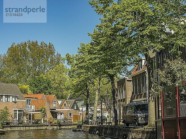 Canal lined with traditional houses and trees  with boats on the water and a clear blue sky  alkmaar  the netherlands