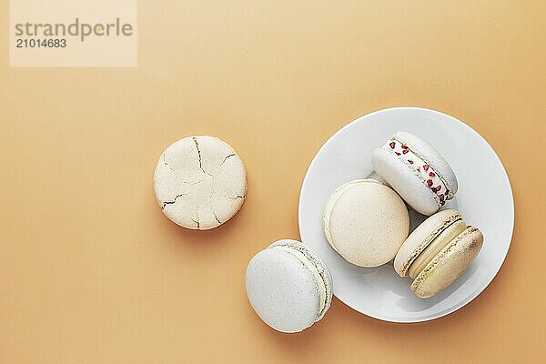 White  yellow  gold macaron cookies. Colorful  sweet small French macaroon cakes. Light yellow background. Broken cut  bitten parts  halves. White plate laying on the table.