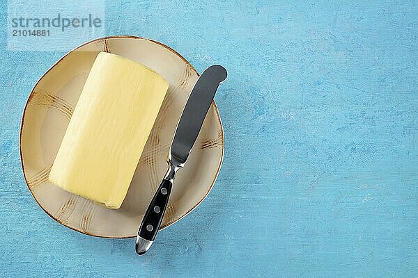 A stick of butter with a knife on a plate  shot from above on a blue background with copy space