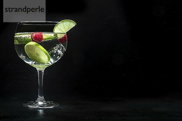 Fancy cocktail with fresh fruit. Gin and tonic drink with ice at a party  on a black background. Alcohol with lime and raspberry  with copy space  Food photography  Food photography