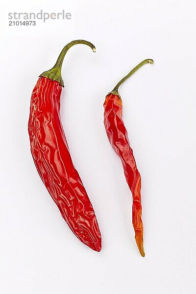 A flatlay studio photo of two dried red peppers set on a white background