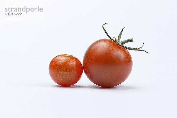 One large and one small cherry tomato set on a white background in a studio setting