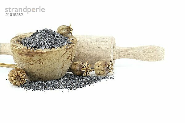 Poppy seeds in wooden bowl and seed pods in front of the rolling pin isolated on white background  full depth of field