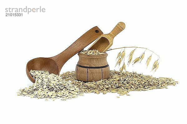 Oat grains with hulls or husks spilling from a wooden barrel and oats groats rolled and flattened into flakes in wooden spoon isolated on white background