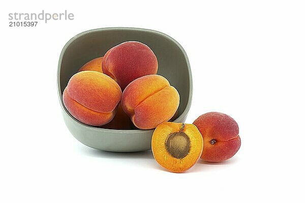 Bowl filled with ripe whole apricots and one cut in half to reveal its interior  isolated on a white background