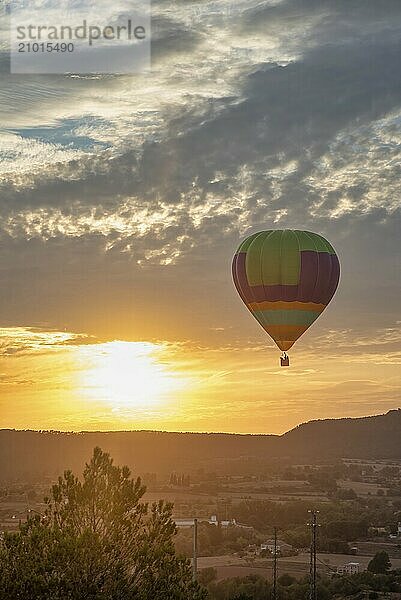 A colourful hot air balloon floats peacefully in a sunset sky with clouds and a hilly landscape