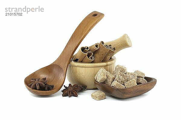 Star anise in a wooden spoon  wooden mortar filled with cinnamon sticks and brown sugar cubes in a wooden bowl isolated on white background