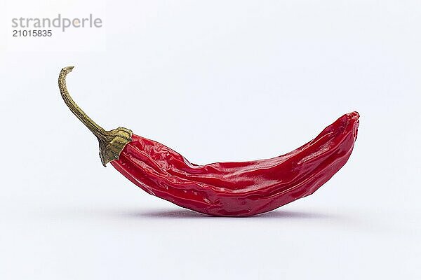 A close up studio photo of a drying red pepper on a white background