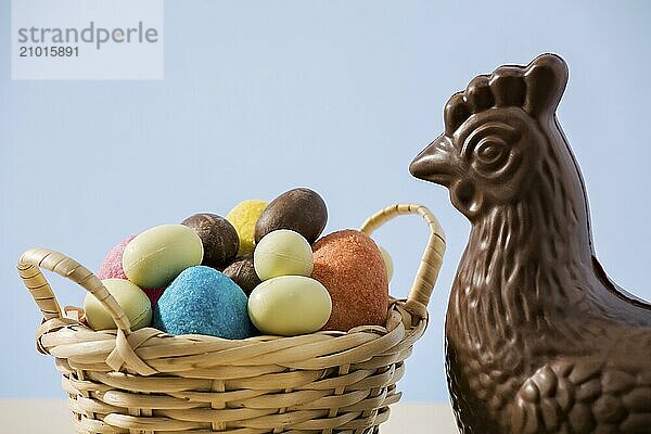 Closeup of easter chocolate chicken and colored eggs in a small basket with blue background