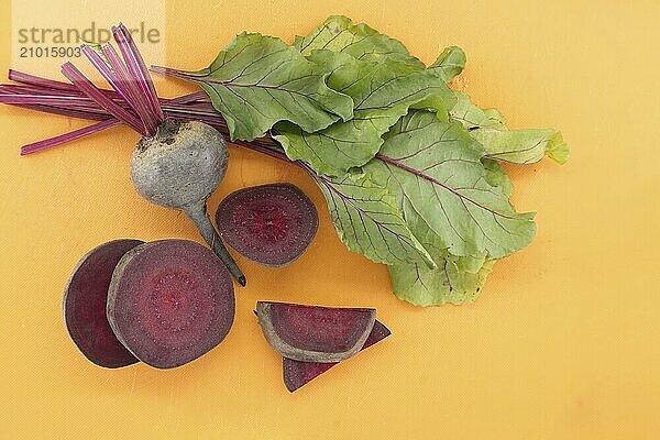 Sliced and whole fresh organic baby beetroot with green leaves on yellow cutting board  top view with free copy space