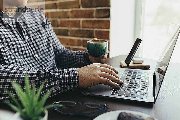 Man working at the laptop with a cup of coffee at home. Blurred background.