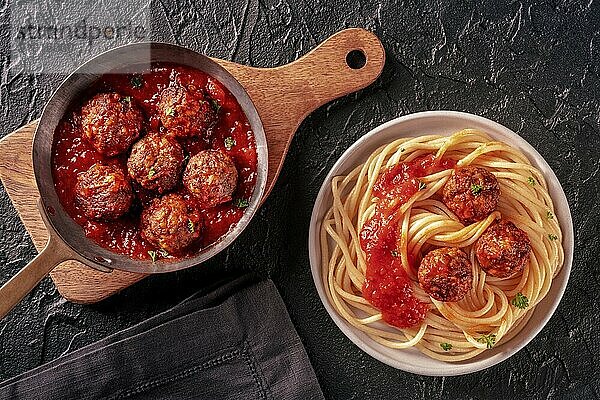 Meatballs. Beef meat balls  overhead flat lay shot in a pan and with a plate of spaghetti pasta  with parsley and tomato sauce  on a black background  Food photography