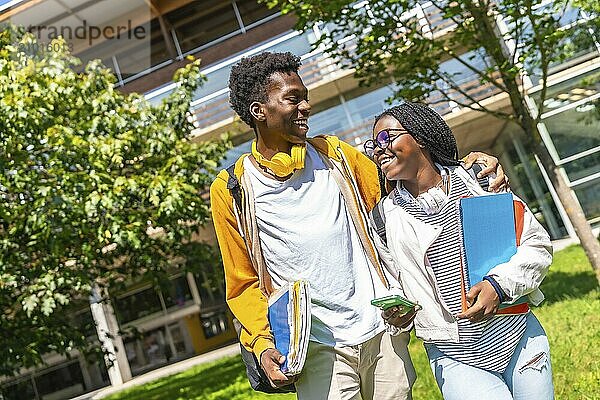 Two happy male and female African friends embracing and chatting walking along the university campus