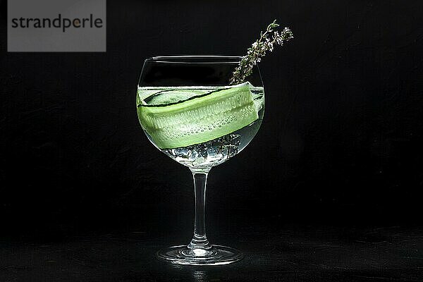 Fancy fresh cocktail. Gin and tonic drink with ice at a party  on a black background. Alcohol with cucumber and thyme