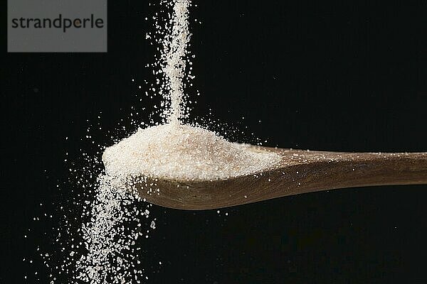 A studio photo of fine himalayan sea salt pouring down on a wooden spoon set against a black background