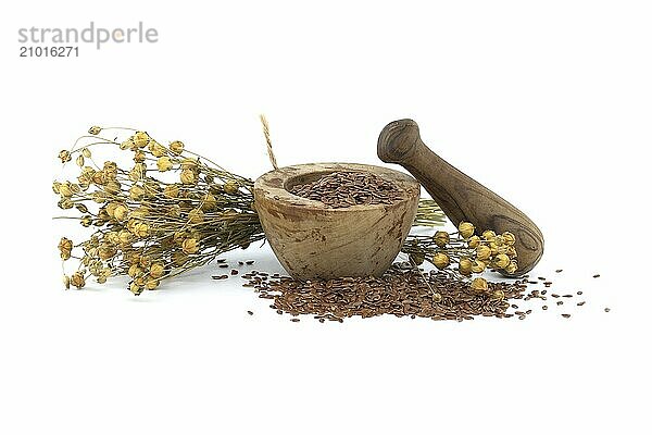 Flaxseed in wooden rustic-style mortar with pestle and bunch of flax plants isolated on white background