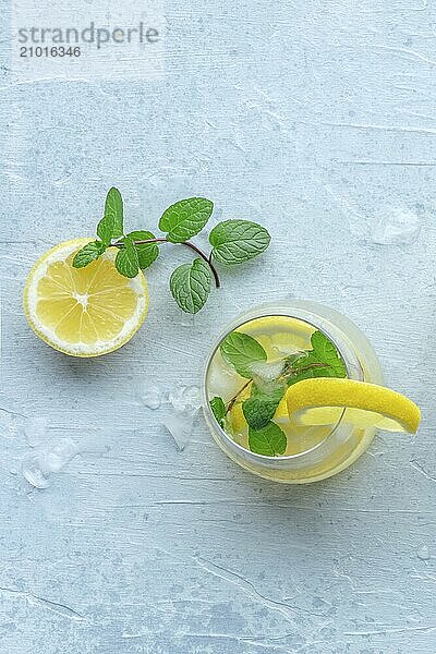 Lemonade with mint. Lemon water drink with ice. A glass and a lemon on a pastel background  overhead flat lay shot. Detox beverage. Fresh homemade cocktail