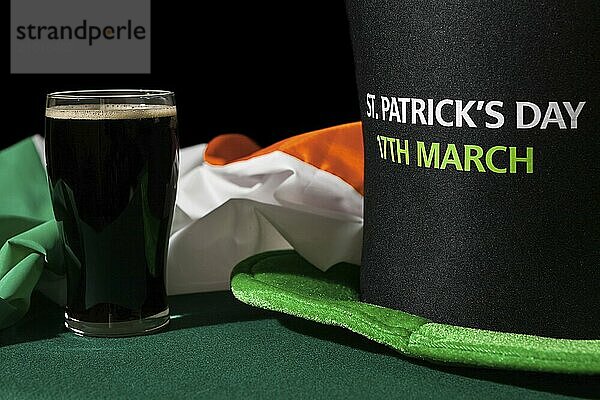 Closeup of St Patrick day with a pint of black beer  hat and irish flag over a green table and black background