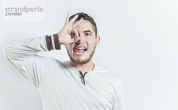 Funny young man making OK gesture looking through fingers isolated. Happy guy making ok gesture looking through fingers