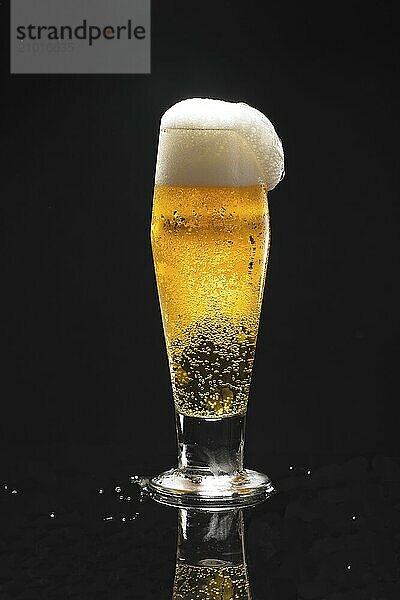 A close up uof a glass of beer against a black background starting to overflow