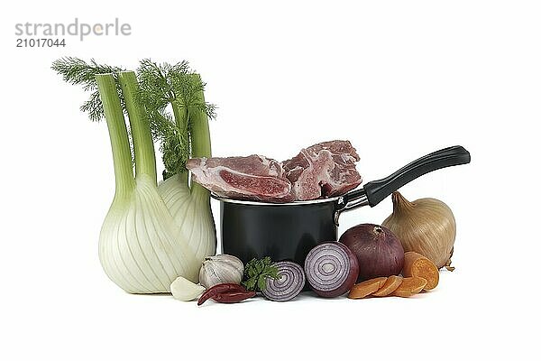 Black saucepan with pieces of raw pork inside. Around the saucepan are sliced vegetables which include onions  carrots  and garlic isolated on white background. Preparation of meat broth