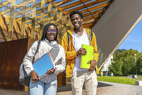 Two male and female young confident african american students walking together along the university campus carrying school bag and folders