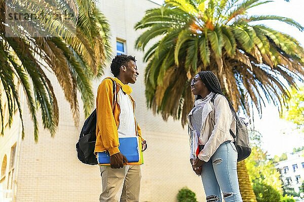 African american university students chatting relaxed after class in the campus next to palm trees