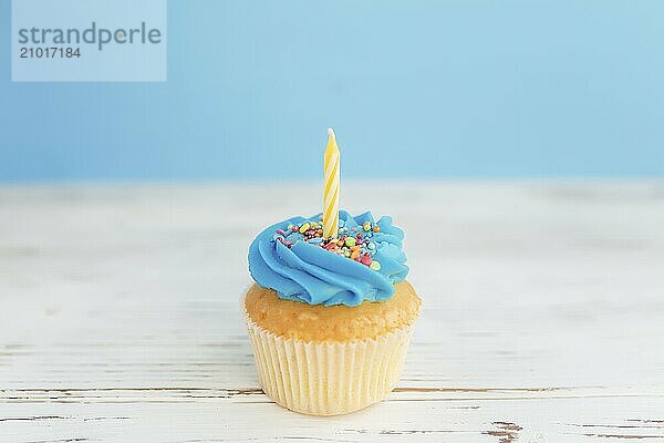 Birthday greetings concept. Yellow candle on a muffin or cupcake. Blue background. Wooden table