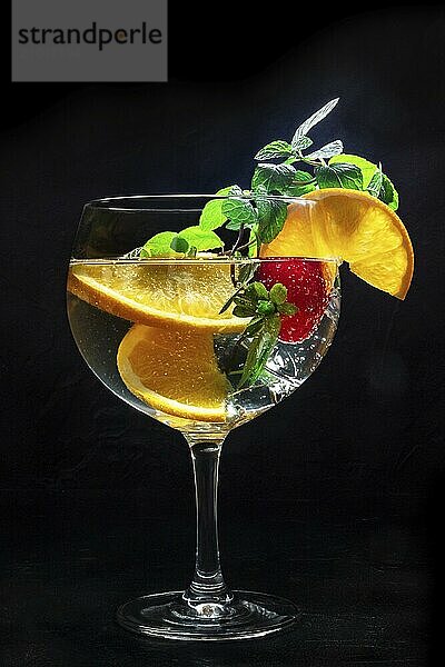 Cocktail with fresh fruit. Gin and tonic drink with ice at a party  on a black background. Alcohol with orange  mint  and strawberry  Food photography