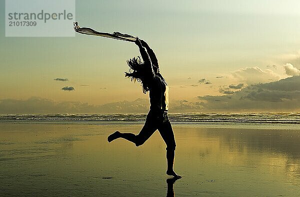 A woman with a scarf leaps on the beach in Newport  Oregon