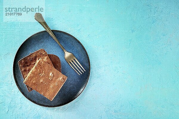 Chocolate brownie  simple coffee cake  overhead flat lay shot on a vibrant blue background  on a plate with a fork  with copy space  Food photography