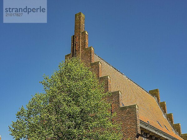 Brick building with a stepped roof and a tree in the foreground against a clear sky  alkmaar  the netherlands