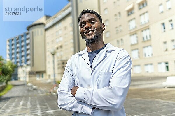 Portrait of an african doctor smiling at camera with arms crossed outside the hospital