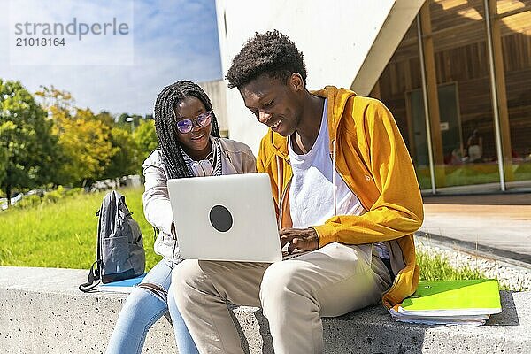 Cheerful african american students using laptop studying together outside the campus