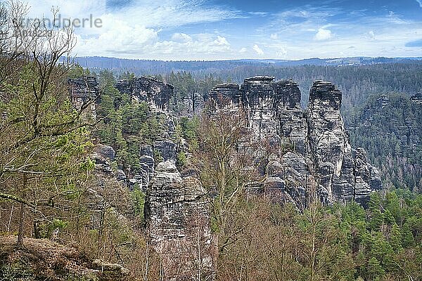 Jagged rocks at the Basteibridge. Wide view over trees and mountains. Dramatic sky. National park in Germany