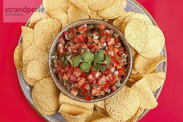 A view from above of chips and homemade salsa on a red background