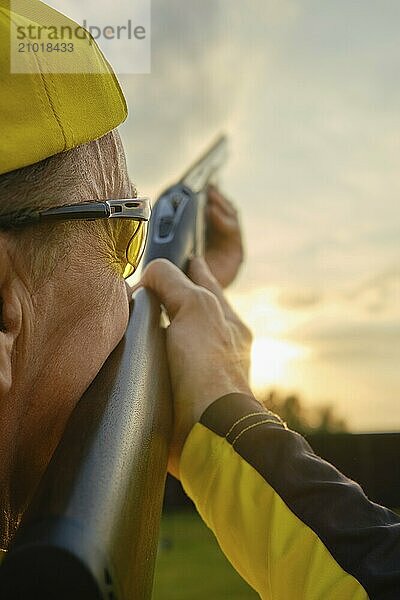 Close-up of a shooter aiming a shotgun at a target during a golden sunset