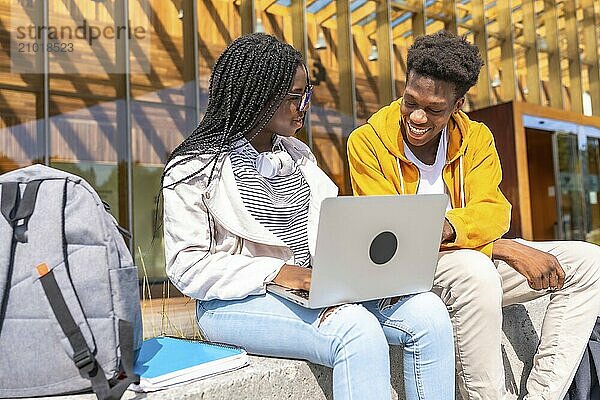 Young african american university friends using laptop sitting outside the campus in a sunny day