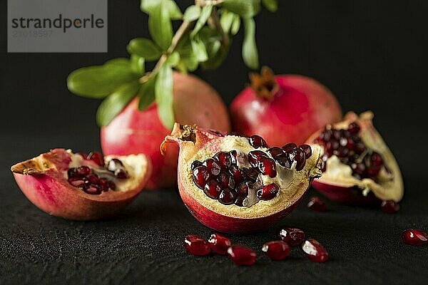 Closeup of ripe pomegranate fruits and seeds over a textured black background