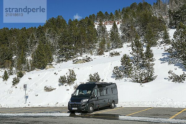 Ein Wohnmobil steht auf einem verschneiten Parkplatz inmitten von Bäumen und Bergen bei kaltem Wetter  Skigebiet  Grandvalira Skiresort  Pas de la Case  Pyrénées-Orientales  Encamp  Fürstentum Andorra  Pyrenäen