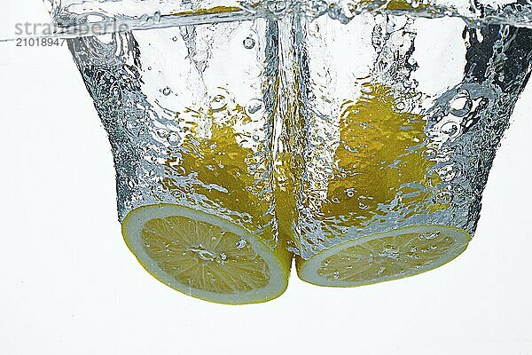 Two lemon halves are dropped into water against a white background